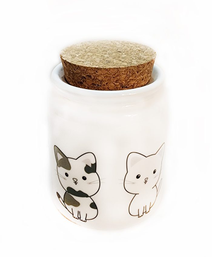 A white jar with cats on it and cork lid.