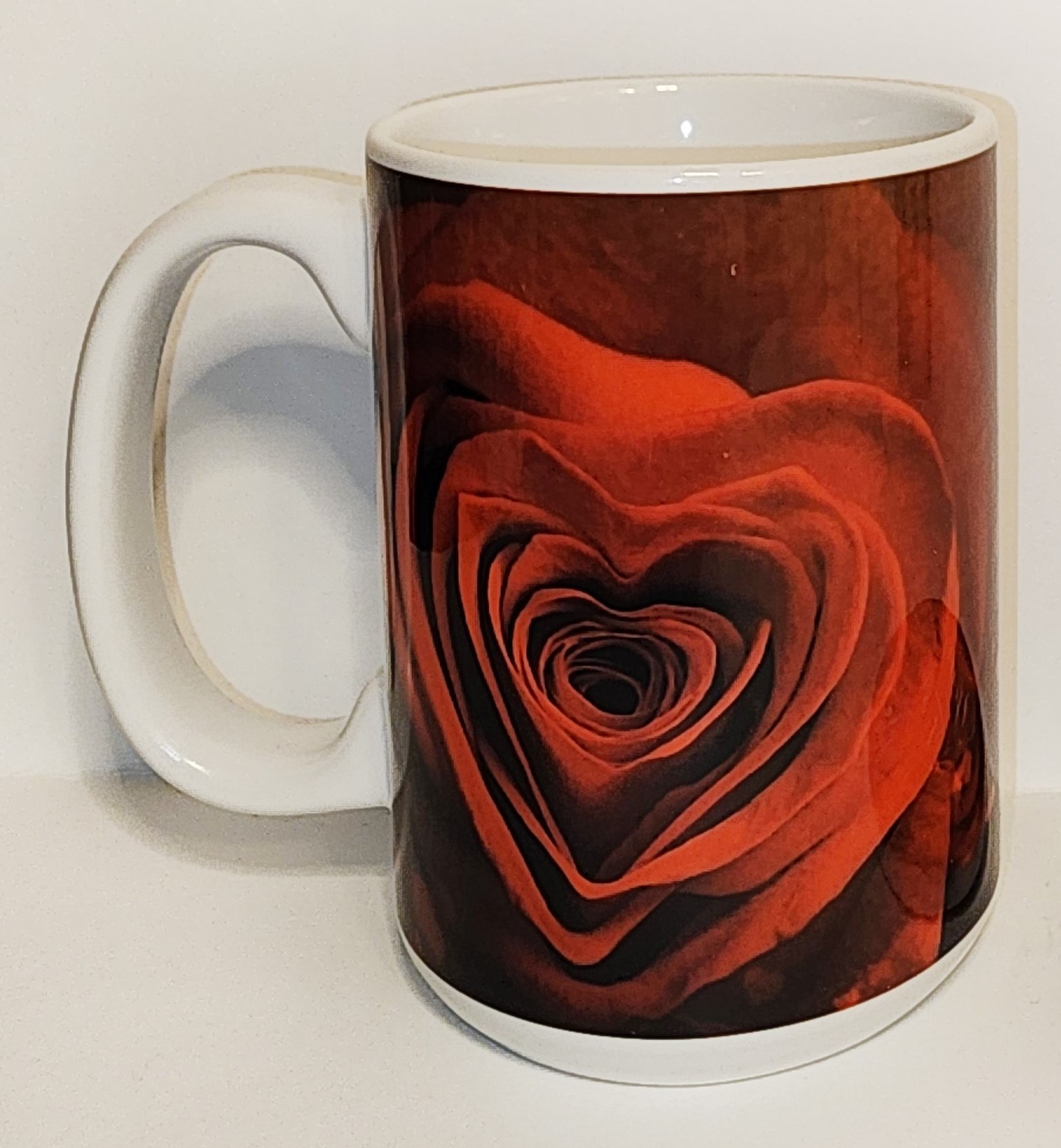 A coffee mug with a heart shaped rose on it.